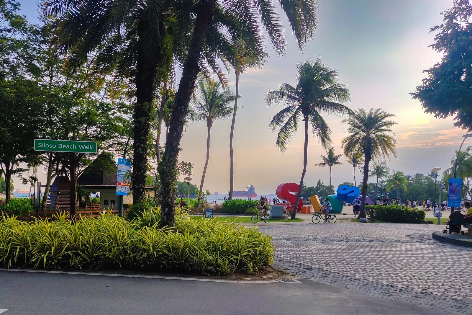 La passeggiata di Siloso Beach a Sentosa, con palme da cocco, un cartello e un sentiero pavimentato che costeggia la spiaggia