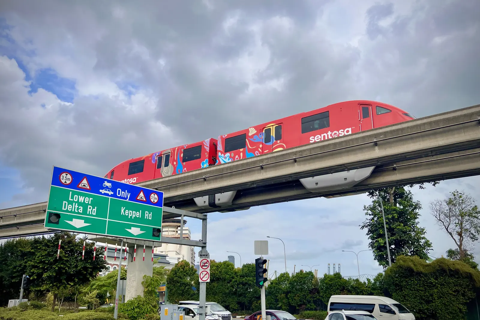 Un treno monorotaia rosso del Sentosa Express sulla sua linea sopraelevata sopra un incrocio stradale, sotto un cielo nuvoloso